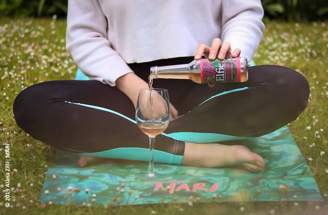 Close up of Elfie Drink being poured into wine glass by model on Yoga Mat. ©2019 Alana Zilli, MARi.